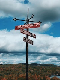 a directional sign on top of a mountain overlooking a lake