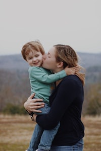 a mother kissing her son in a field