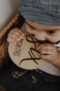 a baby wearing a hat and a hat is chewing on a wooden plate