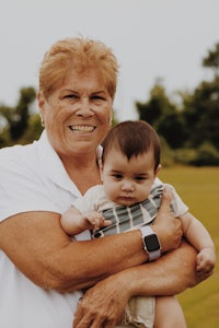 an older woman holding a baby in a field