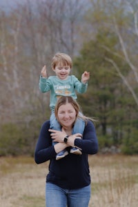 a woman holding a child in a field with mountains in the background