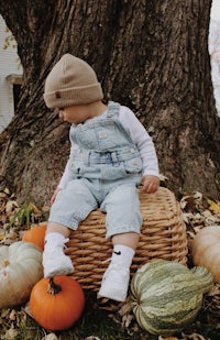 a baby sitting on a wicker basket in front of pumpkins