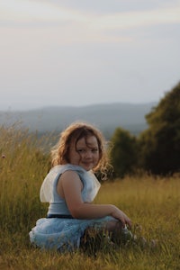 a girl in a blue dress sitting in a field