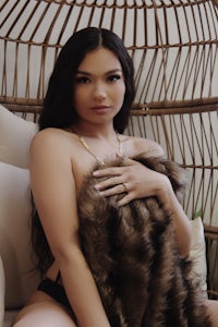 a woman sitting on a wicker chair with a furry blanket