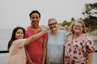 four women posing for a photo with the ocean in the background