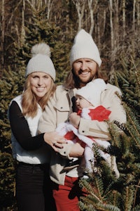 a man and woman holding a baby in a christmas tree farm