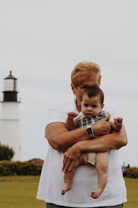 a woman holding a baby in front of a lighthouse