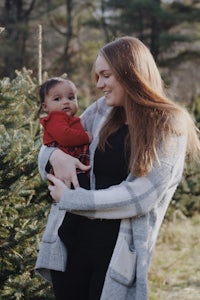 a woman holding a baby in front of a christmas tree farm