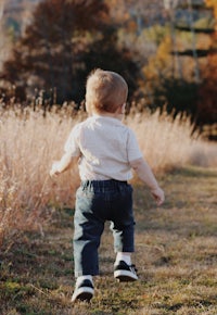 a toddler running through a field with tall grasses