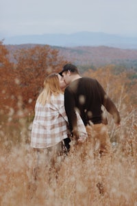 a couple kissing in a field with mountains in the background