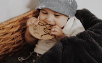 a baby is chewing on a wooden plaque in a basket