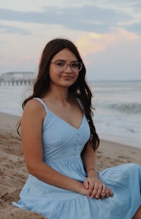 a girl in a blue dress sitting on the beach