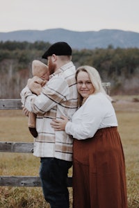 a couple holding a baby in a field with mountains in the background