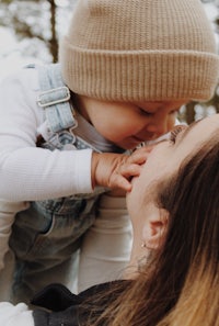 a woman kisses her baby while holding a hat