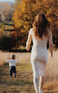 a woman in a white dress running with a child in a field