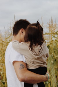 a man holding a child in front of a corn field