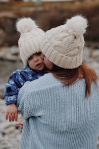 a woman holding a baby while wearing a hat