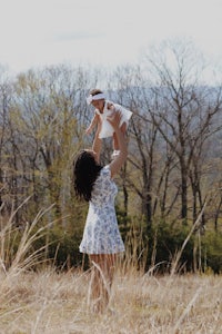 a woman is holding her baby in the air in a field