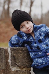 a young boy in a blue jacket leaning against a stone wall