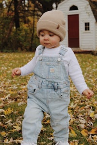 a baby boy wearing overalls and a beanie