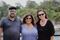 three people posing for a picture near a body of water