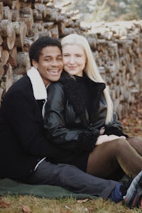 a man and woman sitting on a blanket in front of a pile of logs