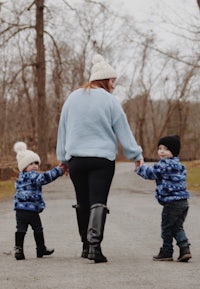 a woman holding hands with two small children walking down a path