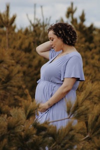 a pregnant woman in a blue dress standing in a pine forest