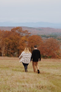 a couple walking through a field with mountains in the background