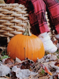 a child is sitting on a wicker basket with a pumpkin