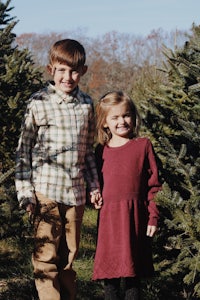 two children standing in front of a christmas tree farm