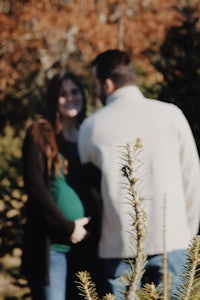 a pregnant couple standing in front of a christmas tree farm