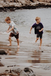 two boys running on a beach near the water