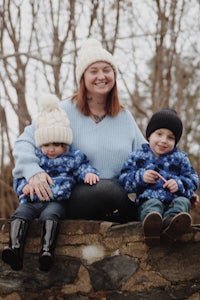 a woman and two children sitting on a stone wall