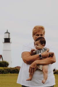 a woman holding a baby in front of a lighthouse