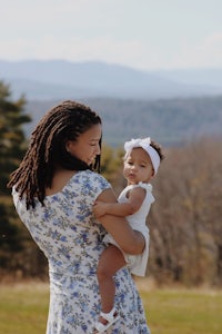 a woman holding a baby in a field with mountains in the background