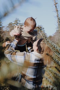 a woman holding a baby in the air in a christmas tree field