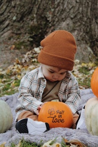 a baby sitting on a blanket with pumpkins and a hat