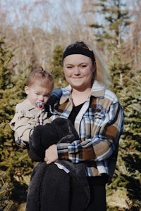 a woman holding a baby in front of a christmas tree farm