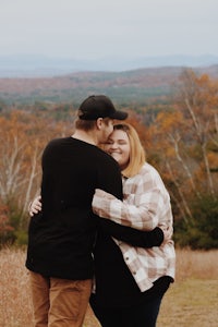 a couple embraces in the middle of a field with mountains in the background