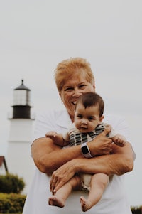 a woman holding a baby in front of a lighthouse