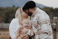 a man and woman kissing their baby in front of a fence