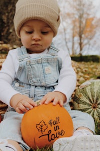 a baby is playing with a pumpkin in the grass