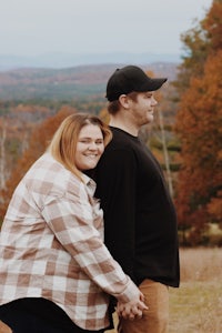 a couple standing in a field with trees in the background