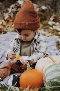 a baby sitting on a blanket with pumpkins and a beanie