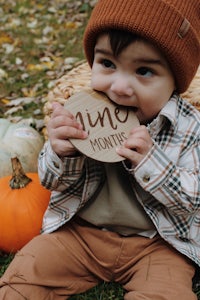 a baby wearing a hat and a hat eats a wooden pumpkin