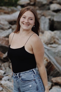 a young woman in a black tank top and jeans standing in front of rocks