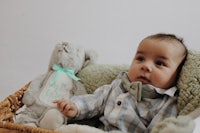 a baby sitting in a wicker basket with a teddy bear