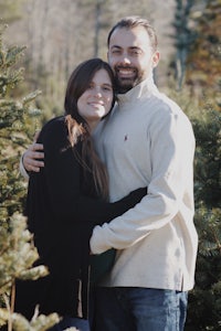 a couple embracing in front of a christmas tree farm