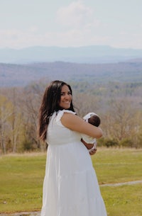 a woman in a white dress holding a baby in a field